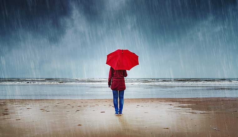 Person with red umbrella is standing in the rain watching the sea