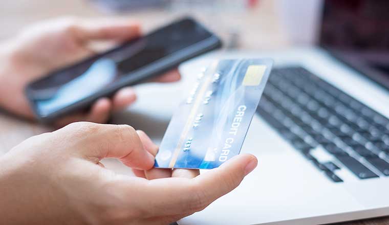 A hand holding credit card with using smartphone and laptop