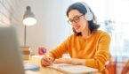 Person making notes with headphones and laptop