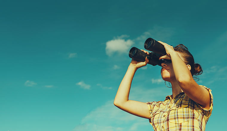 Looking Through Binoculars On Blue Sky Background.