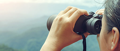 Person looks through binoculars on mountains background