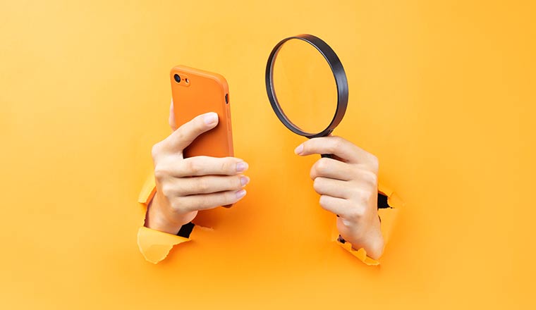 Hand holding magnifying glass and phone protruding from background