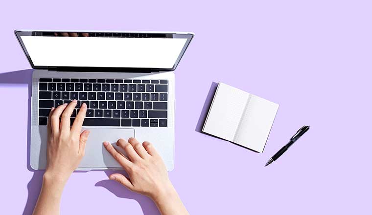 Person using a laptop computer with a notebook and a calculator