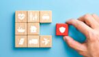 Hand holding red wooden blocks with insurance icons.