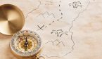 Closeup of compass over stained yellowed paper sheet with part of hand drawn treasure map