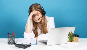 despaired telemarketing worker wearing headset in front of laptop