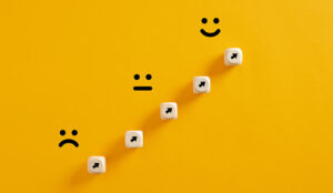 Arrows on wooden cubes pointing from a sad expression towards a happy one.
