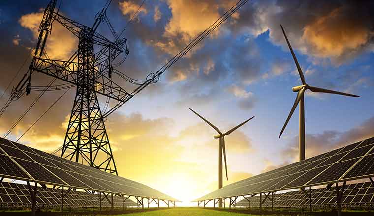 Solar panels with wind turbines and electricity pylon at sunset.