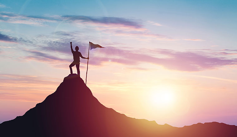 Person with flag celebrates victory on top of a mountain at sunset