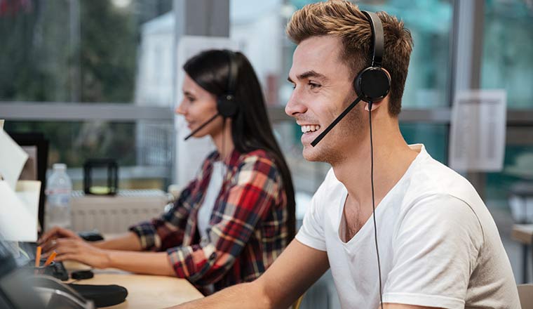 Smiling call centre operators sit by the table in headphones