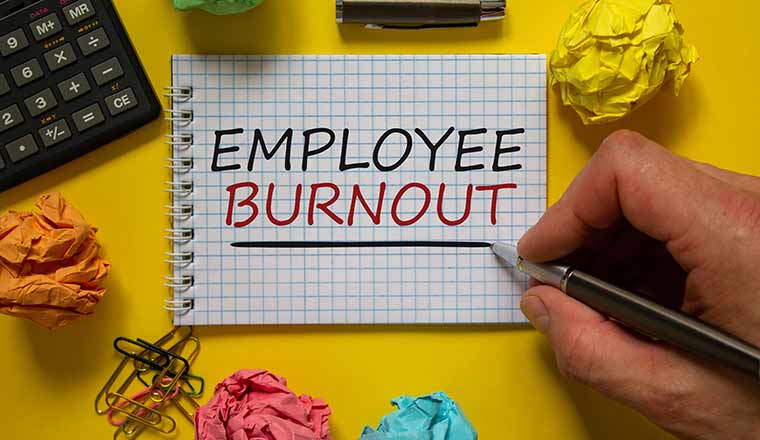 Employee burnout concept, with a hand writing 'Employee burnout' on white note