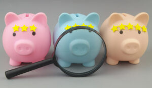 Magnifying glass and piggy banks with yellow stars on gray background.