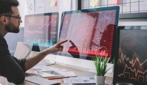 Data analyst pointing with finger at charts on computer monitor while testing computer systems