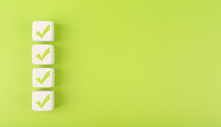 Four checkmarks on white cubes against bright green background - testing results concept