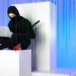 ninja in black clothing using laptop while sitting on white block with code