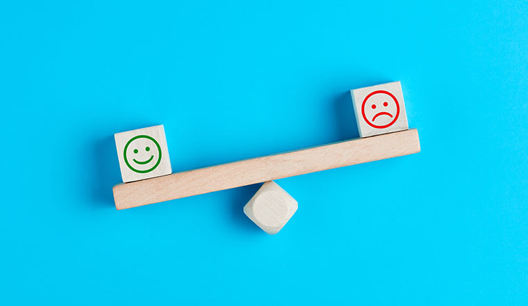 Happy and sad smiley faces on wooden seesaw.