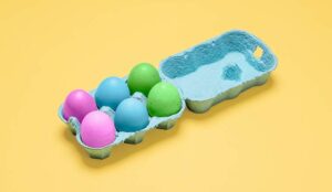 Half dozen easter eggs in egg container on yellow.