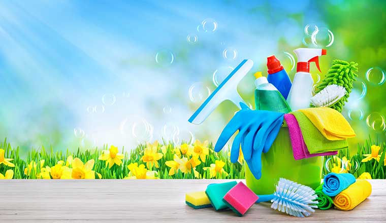 Bucket with cleaning items on blurry spring background with sun beams and soapbubbles