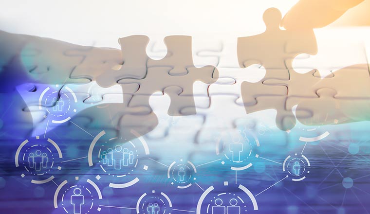 A hand holding jigsaw piece with background of teamwork people connection - technology solving staffing gaps concept