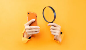 Hand holding magnifying glass and phone protruding from background