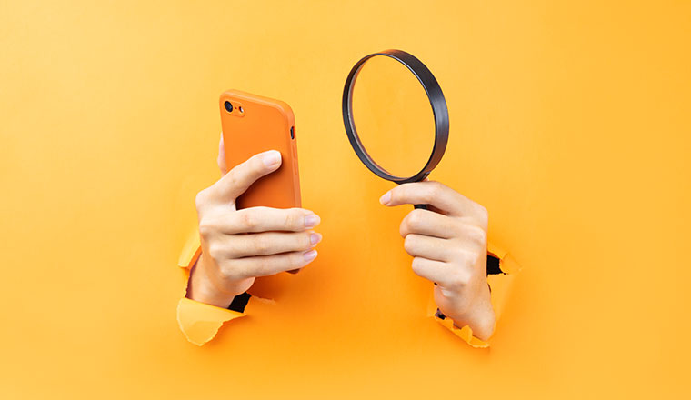 Hand holding magnifying glass and phone protruding from background