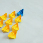 Leadership concept with paper boats on blue wooden background