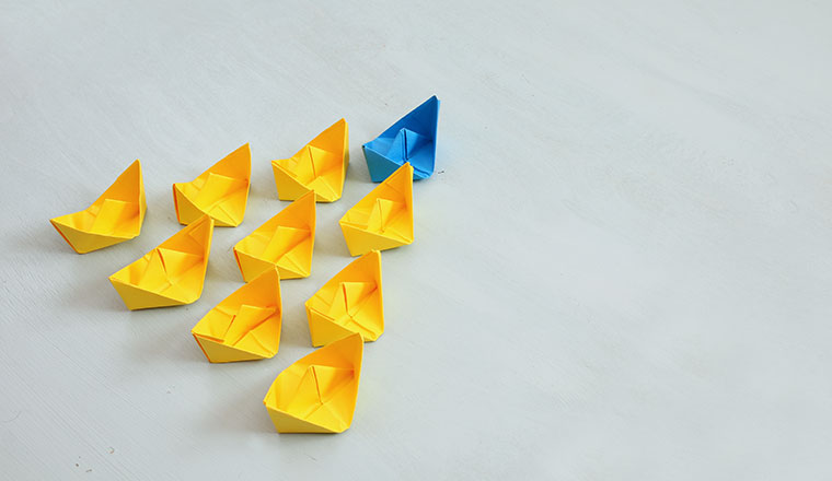 Leadership concept with paper boats on blue wooden background