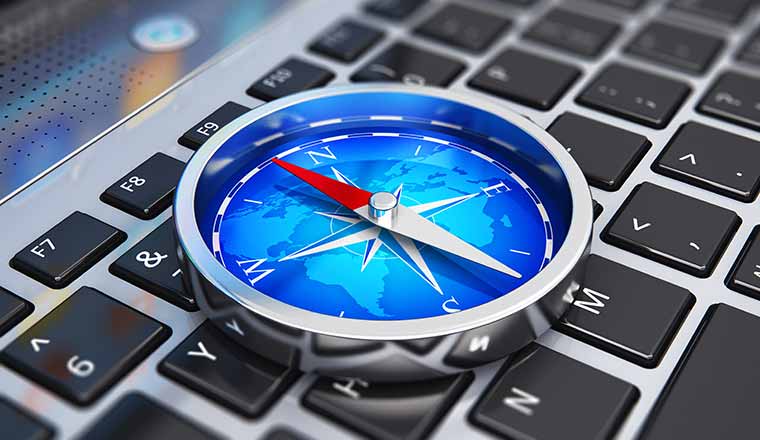 A compass with red arrow and blue world map on laptop