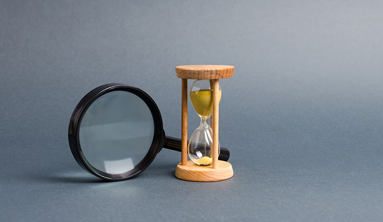 Magnifying glass and hourglass. Search for time and resources.
