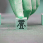 Selective focus on hand pushing a wooden cube with a robot. In a blurred background, two cubes with human icon. AI bridging gap