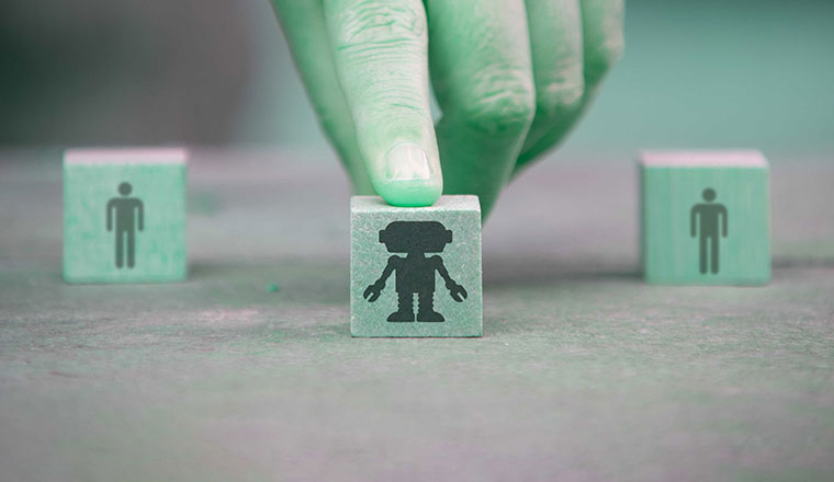 Selective focus on hand pushing a wooden cube with a robot. In a blurred background, two cubes with human icon. AI bridging gap