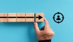 Wooden blocks with the arrow moving towards the target customer symbol.