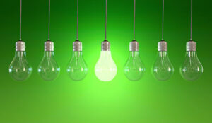 Seven light bulbs with lit one on green background