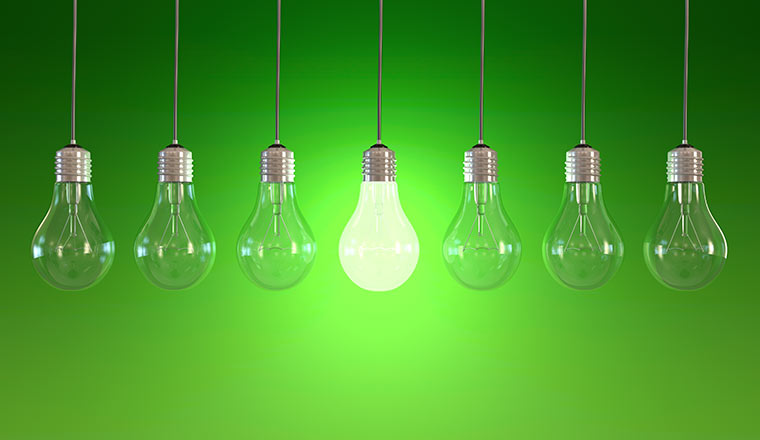 Seven light bulbs with lit one on green background