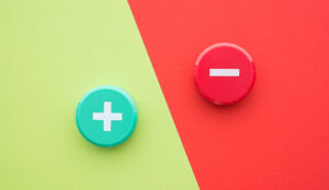 Flat lay of green plus and red minus symbol plastic button on green and red background