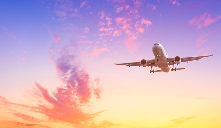 Airplane flying above dramatic clouds during sunset