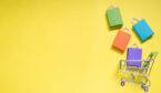 Retail concept with Trolley cart and colorful paper shopping bags on yellow background.
