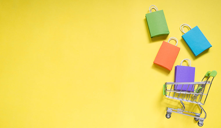 Retail concept with Trolley cart and colorful paper shopping bags on yellow background.