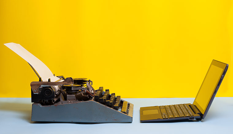 Old typewriter and laptop on table on yellow background. Concept of technology progress. Old vs new