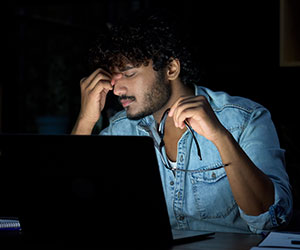 Overloaded person sat at desk rubbing their face