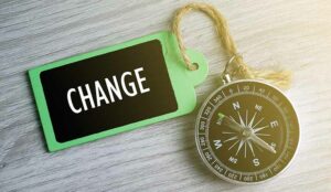 Compass and wooden tag written with CHANGE on grey background.