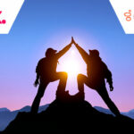 Two people standing at top of mountain giving high five - partnership concept