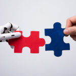 Close-up Of Robot And Human Hand Holding Red And Blue Jigsaw Puzzle - partnership concept
