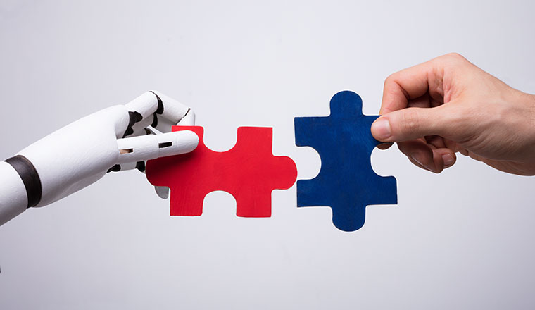 Close-up Of Robot And Human Hand Holding Red And Blue Jigsaw Puzzle - partnership concept