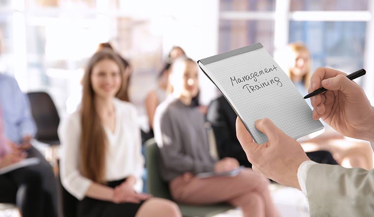 A trainer holding notebook with text MANAGEMENT TRAINING at presentation