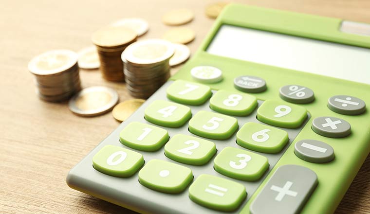 Green calculator with coins on wooden table