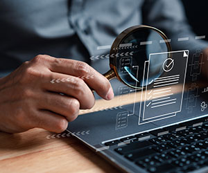 Person at laptop with magnifying glass reviewing data