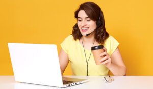 Person sat at their desk with a computer and coffee with a yellow background.