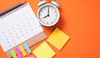 Close up of alarm clock and calendar on the orange table background.