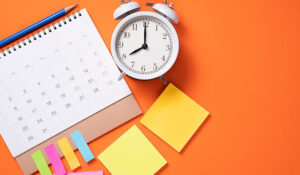 Close up of alarm clock and calendar on the orange table background.